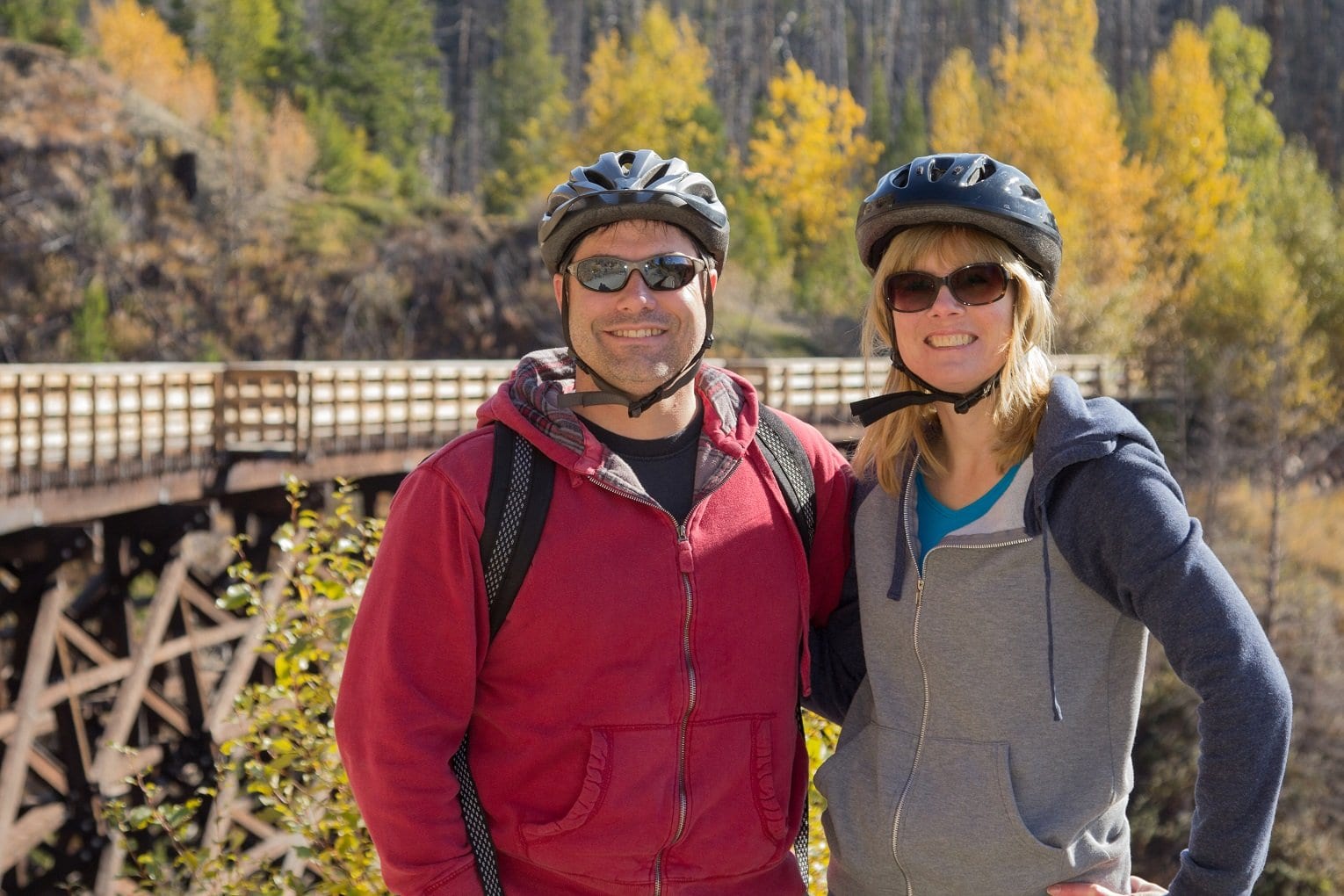 male and female couple in biking gear standing in front of myra canyon trestles high end real estate Kelowna